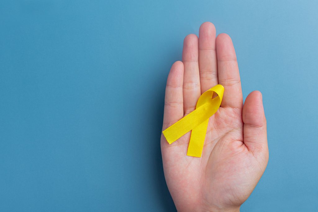 Hands holding yellow ribbon, symbol of cancer awareness, medical