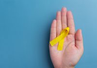 Hands holding yellow ribbon, symbol of cancer awareness, medical